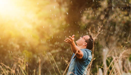 uomo sorridente fuori con le braccia tese verso la luce con gocce di pioggia che cadono su di lui