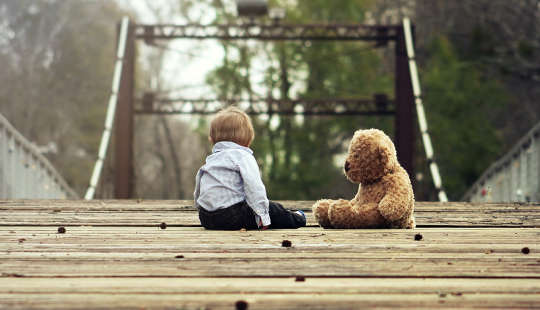 ילד צעיר יושב על גשר עם הדובון שלו