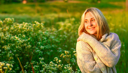 en smilende kvinde i en mark med blomster, der giver sig selv et kram