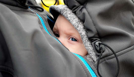 एक बच्चा अपनी माँ की जैकेट के अंदर उसकी छाती पर छिपा हुआ है
