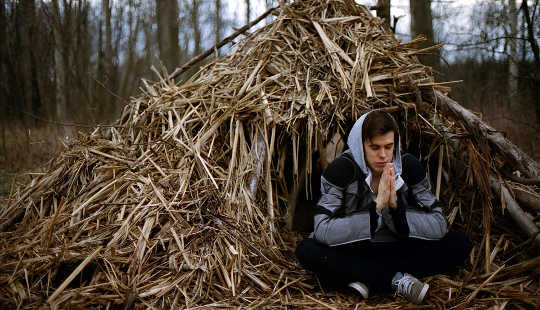 young man meditating in front of a straw shelter