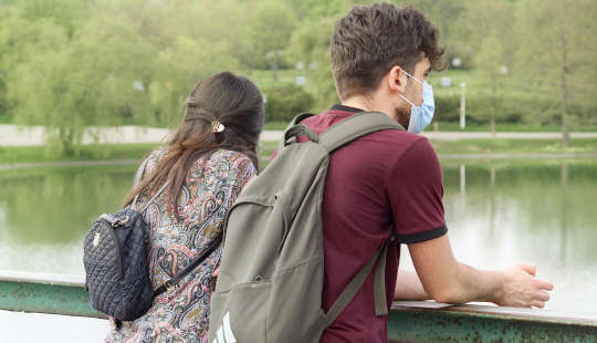 a young couple, wearing protective masks, standing on a bridge