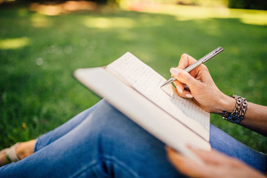 een persoon die buiten op het gras zit en in een notitieboekje schrijft