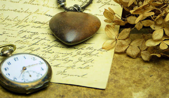 eine Taschenuhr und ein Herzanhänger, die auf einem handgeschriebenen Brief liegen