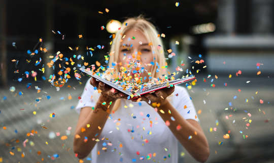 woman blowing confetti off of an open book