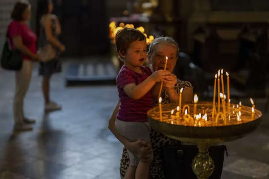 seorang nenek membantu cucunya menyalakan lilin di sebuah gereja di Lviv