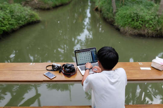 un niño en un barco con su computadora portátil abierta y una cámara y un teléfono celular a su lado.