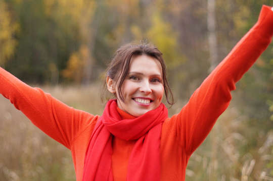 улыбающаяся молодая женщина, одетая в красное, с поднятыми руками в знак победы