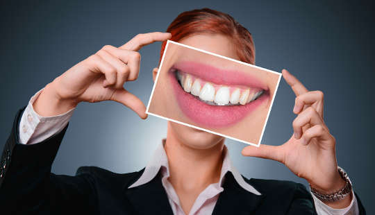 een vrouw die een vergrote foto van haar tanden omhoog houdt