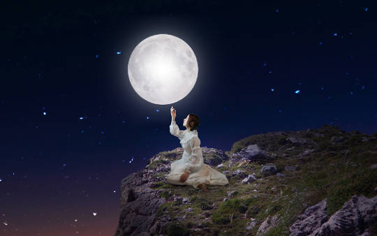 wanita duduk di bawah bulan purnama dan bintang
