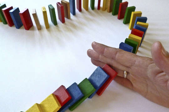 en hånd som holder tilbake en barrikade av dominobrikker fra å falle