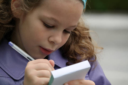 seorang gadis muda dengan penuh perhatian menulis di secarik kertas
