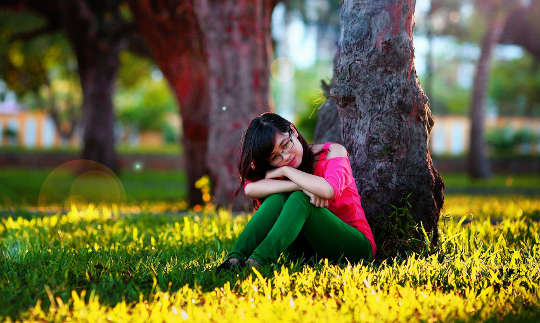 una giovane donna seduta e in appoggio contro un albero