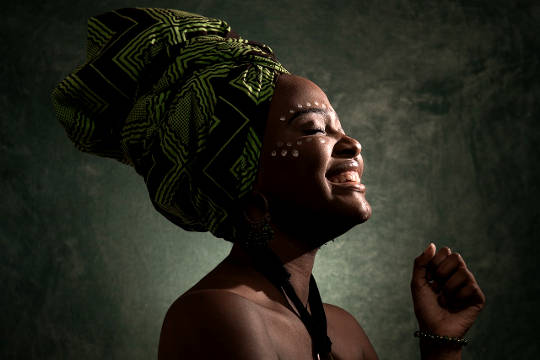 افریقی عورت ہیڈ ڈریس پہنے آنکھیں بند کر کے مسکرا رہی ہے۔