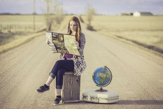 一位年輕女子坐在路中間的手提箱上，旁邊有一個地球儀
