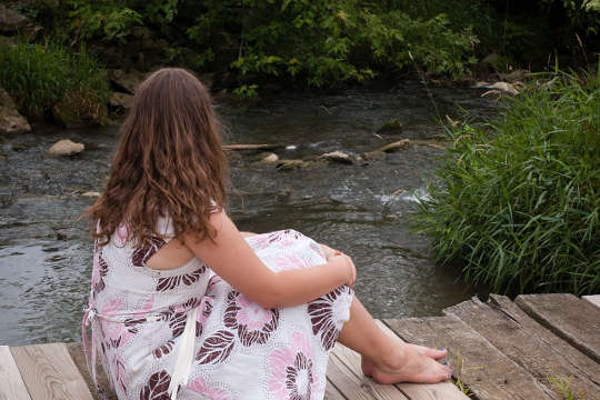 امرأة شابة حافية القدمين تجلس على جسر تطل على النهر