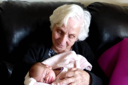 en mormor (eller kanske en gammelmormor) som håller i ett nyfött barn