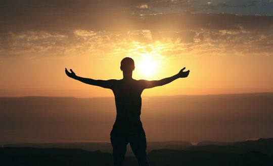 o persoană cu brațele larg deschise în fața soarelui care răsare