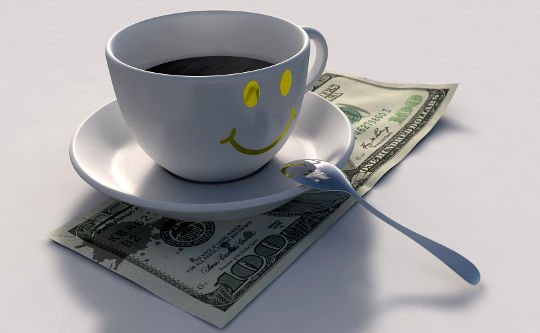 o ceașcă cu fața zâmbitoare cu cafea peste o bancnotă de 100 USD
