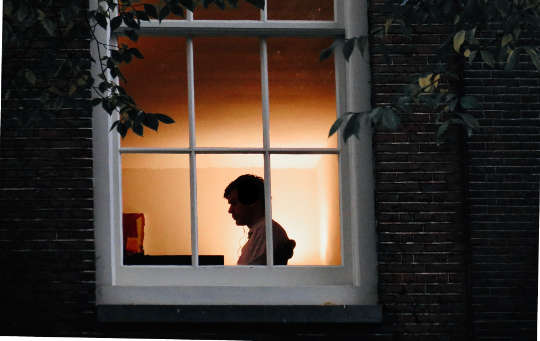 person som sitter alene i et hus, sett gjennom et vindu