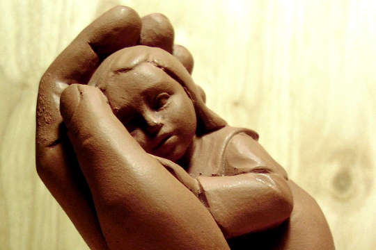 isang clay sculpture ng isang bata na hawak sa isang supportive na kamay