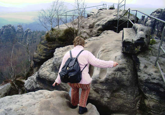 older woman wearing a backpack climbing a rocky path
