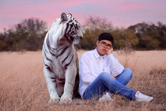 jovem sentado em um campo com um grande tigre sentado ao lado dele