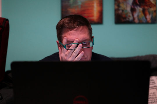 en man som sitter framför en datorskärm och gnuggar sig i ögonen