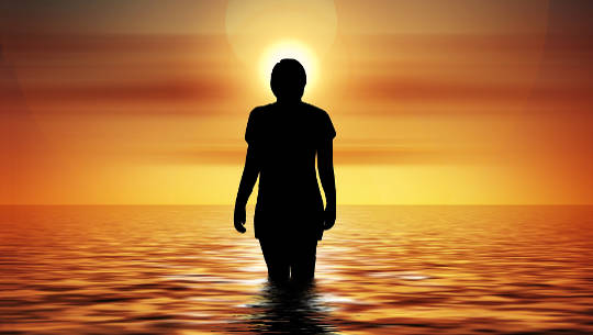 жінка, що стоїть в океані, дивлячись на сонце, що сходить