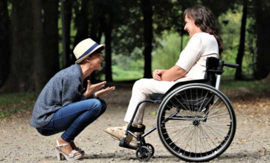 заботливый человек, сидящий на корточках перед другим в инвалидной коляске