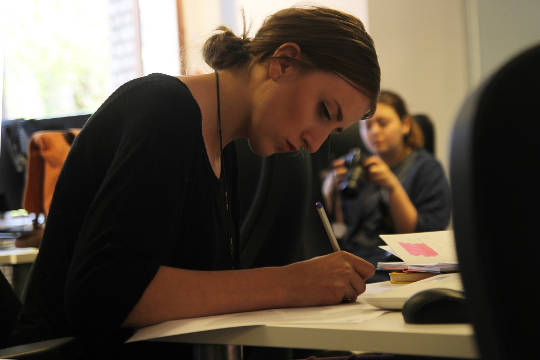 mujer sentada en un escritorio trabajando mientras alguien en el fondo no está trabajando