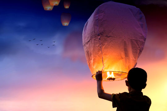 ένα νεαρό αγόρι που απελευθερώνει φωτισμένα μπαλόνια στον ουρανό