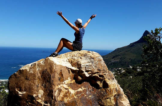 徒步旅行者坐在一块巨大的岩石上，胜利地高举双臂