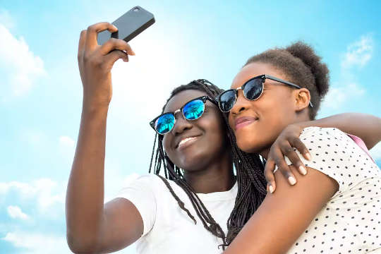 wanawake wawili wakiwa wamekumbatiana wakipiga selfie