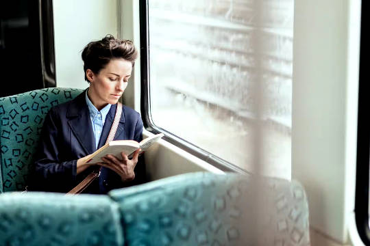 nainen istuu julkisessa liikenteessä lukemassa kirjaa