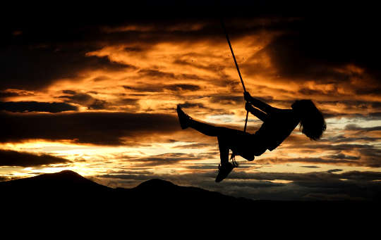 siluett av en flicka på en gunga framför solnedgången