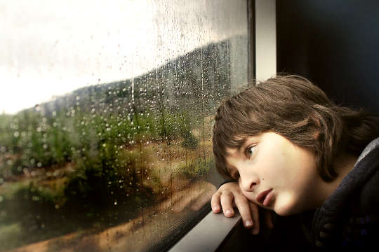 ung pojke tittar eftertänksamt ut genom ett fönster
