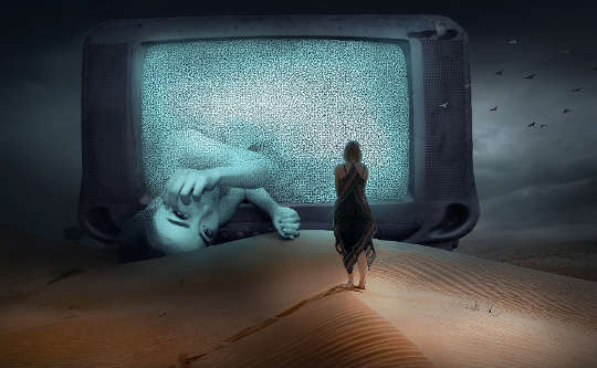 layar tv di padang pasir dengan seorang wanita berdiri di depan dan setengah jalan keluar dari layar