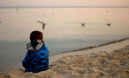 un bambino seduto su una spiaggia che guarda con calma gli uccelli in volo