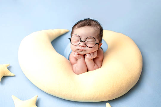 baby med lukkede øjne iført enorme briller og hvilende på en halvmåneformet pillos