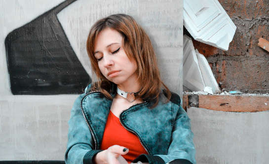 egy kétségbeesett külsejű fiatal nő a fal mellett ül