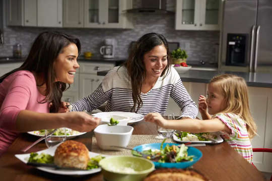 3 Kinder teilen sich eine Mahlzeit und lachen um den Tisch herum