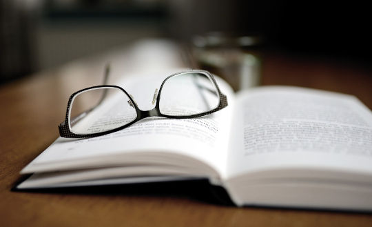 sebuah buku terbuka dengan sepasang cermin mata diletakkan di atasnya