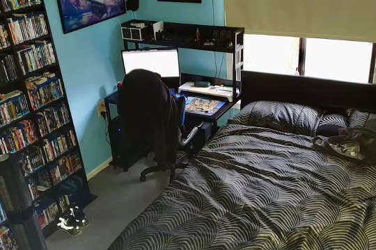 Schlafzimmer mit Computer und Schreibtisch direkt neben dem Kopfende des Bettes
