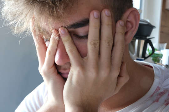 young man with yees closed and with his face in his hands