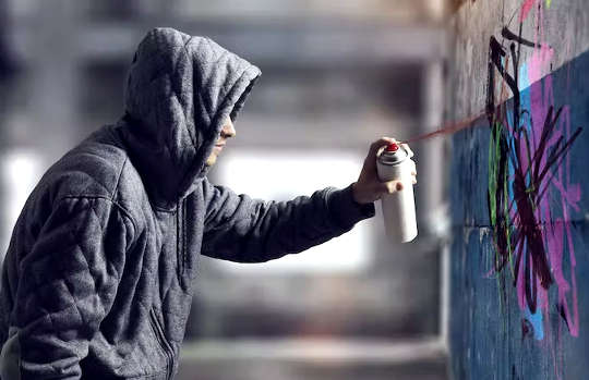 גבר צעיר לובש קפוצ'ון מרסס גרפיטי על קיר