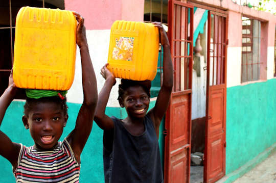 頭にバケツの水を載せて喜んでいる XNUMX 人のアフリカの子供たち