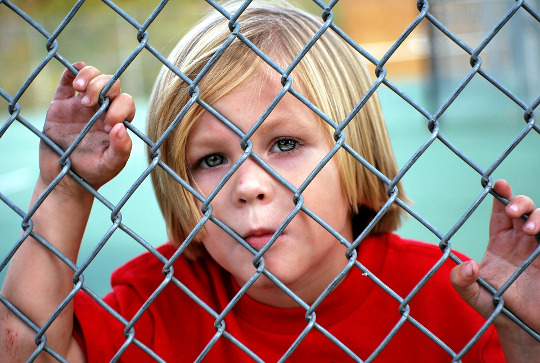 一個小男孩從鐵絲網圍欄後面往外看