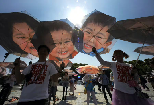 People hold umbrellas with portraits of young survivors of the earthquake and tsunami that hit eastern Japan on March 11, 2011.