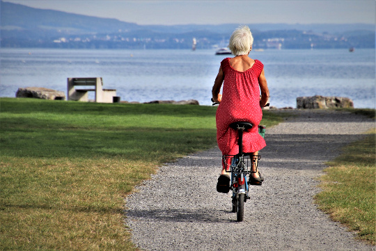 một người phụ nữ lớn tuổi với mái tóc trắng và chiếc váy đỏ đi xe đạp